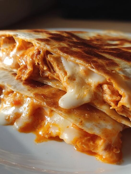 Close-up of two halves of Buffalo Chicken Quesadillas stacked, showing shredded chicken and melted cheese oozing out.