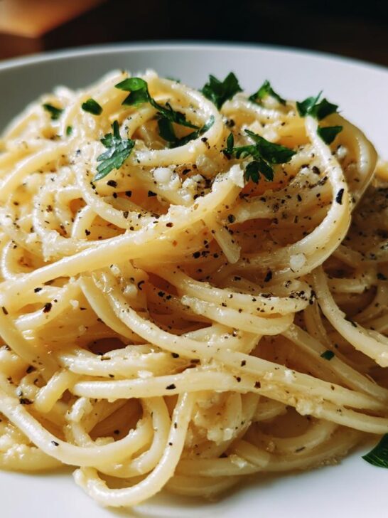 A close-up shot of perfectly coated Buttery Garlic Noodles, seasoned heavily with black pepper and topped with fresh parsley.