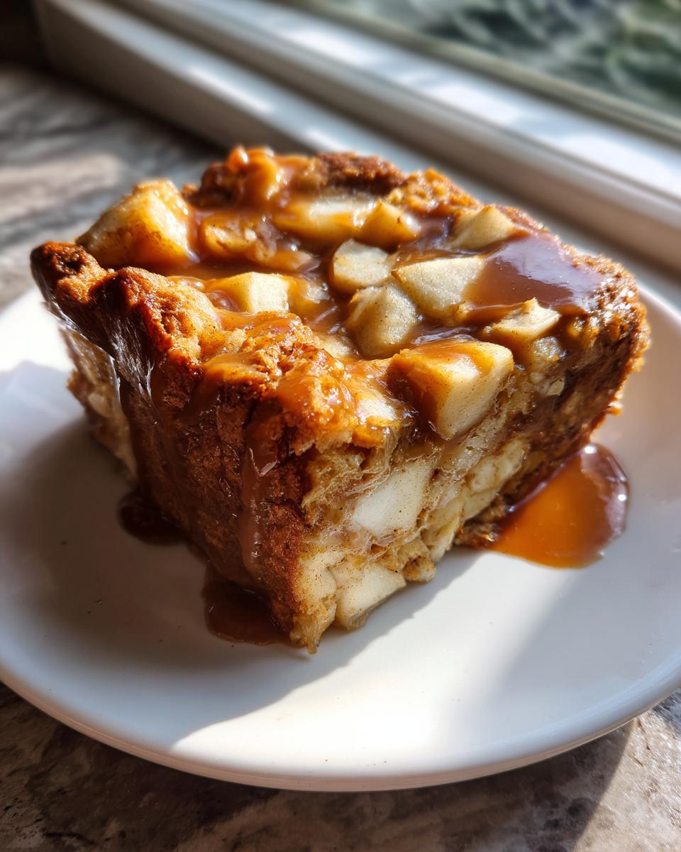 A close-up of a square serving of Caramel Apple Stuffed French Toast Casserole topped with chunks of apple and rich caramel sauce.