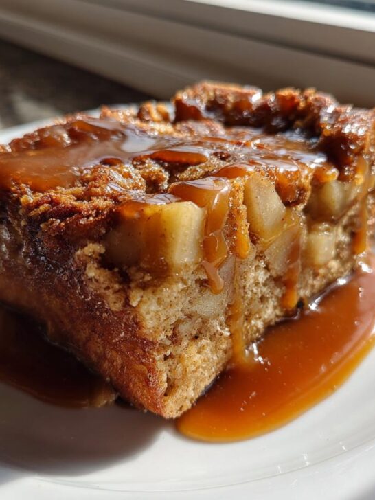 A close-up of a square slice of Caramel Apple Stuffed French Toast Casserole topped with rich caramel sauce.