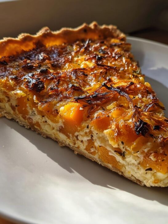 A golden slice of Caramelized Onion Butternut Squash Tart featuring bright orange squash chunks and dark caramelized onions on a white plate.