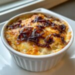 Close-up of a baked Caramelized Onion And Gruyere Dip topped with browned cheese and dark caramelized onions in a white ramekin.