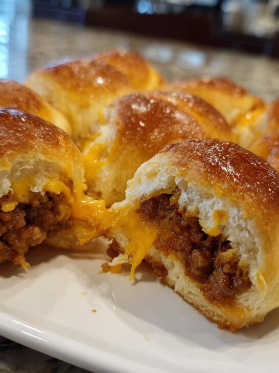 Close-up of freshly baked Cheeseburger Bomb Bites, one is broken open showing seasoned ground beef and melted cheddar cheese.