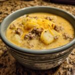 A close-up of a bowl of creamy Cheeseburger Soup With Potatoes, topped with ground beef and shredded cheddar cheese.
