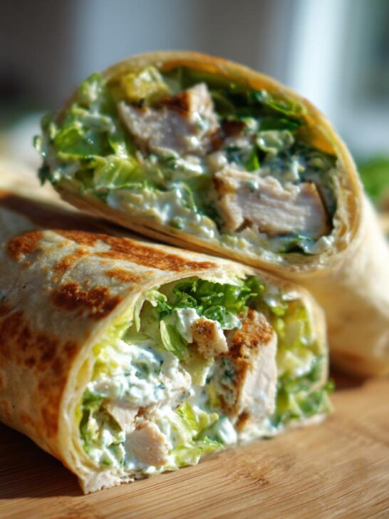 Two halves of a toasted Chicken Caesar Salad Wrap showing grilled chicken, crisp lettuce, and creamy dressing.