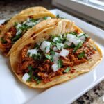 Two delicious Chicken Street Tacos filled with shredded chicken, topped with diced white onion and fresh cilantro.