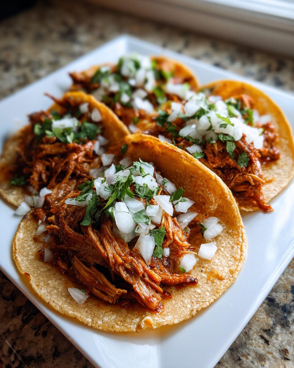 Close-up of three delicious Chicken Street Tacos filled with shredded seasoned chicken, topped with diced white onion and fresh cilantro.