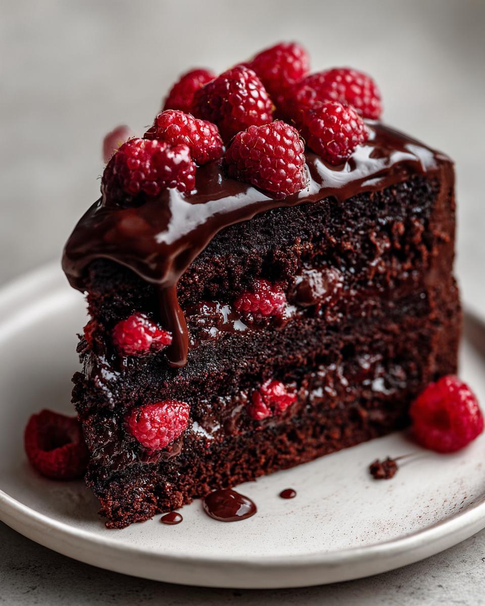 A decadent slice of Chocolate Cake With Chocolate Ganache And Raspberries, topped with fresh berries.
