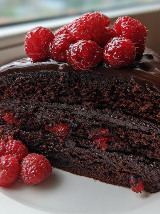 A rich slice of Chocolate Cake With Chocolate Ganache And Raspberries, layered and topped with fresh berries.
