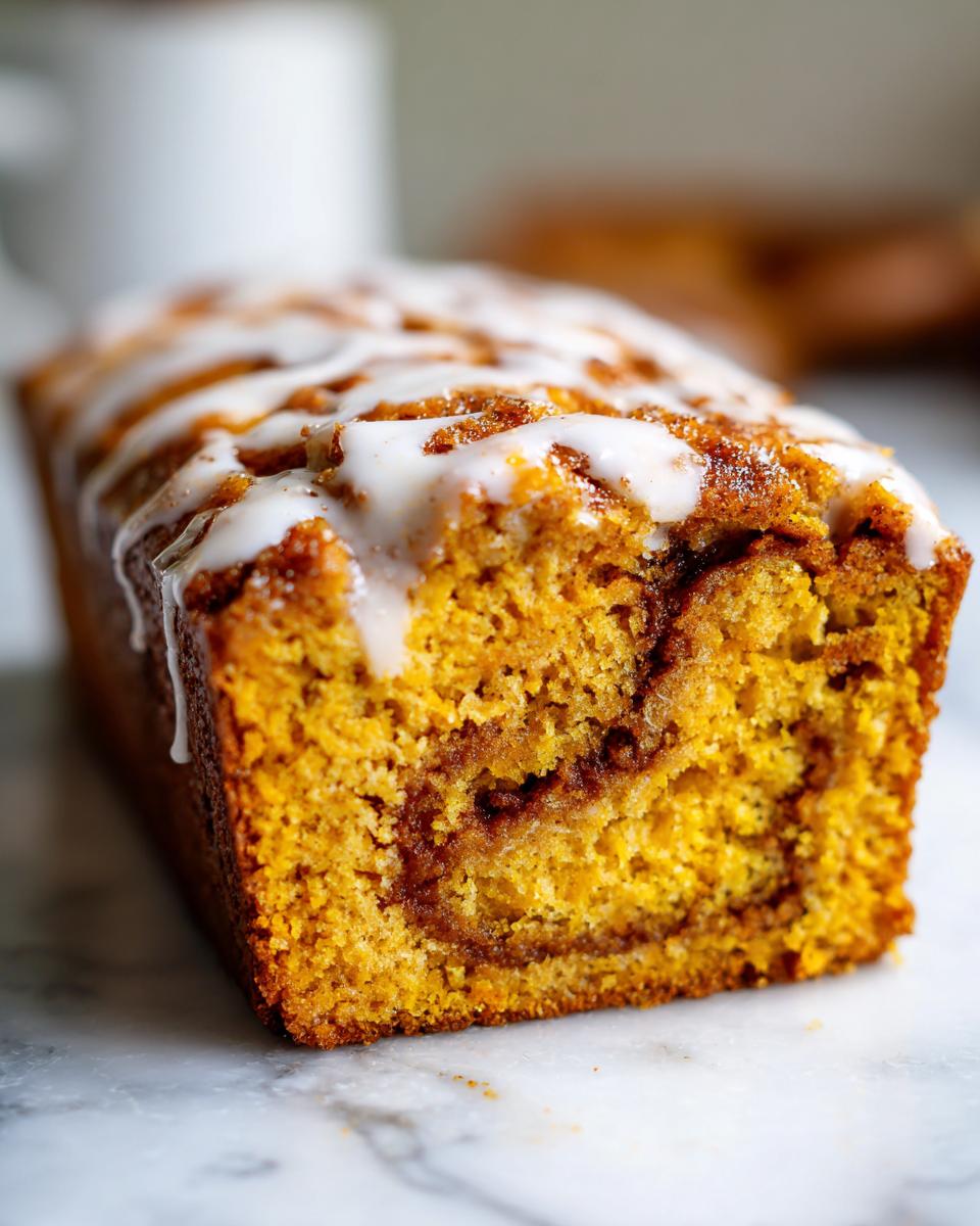 Close-up of a freshly baked Cinnamon Roll Pumpkin Bread loaf with a thick vanilla glaze drizzle.
