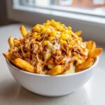A white bowl filled with a Copycat KFC Famous Bowl featuring french fries, mashed potatoes, shredded chicken, corn, and gravy.