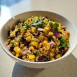 Close-up of a white bowl filled with vibrant Corn And Black Bean Quinoa Salad, topped with cilantro.