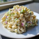 A mound of creamy Greek Yogurt Macaroni Salad featuring elbow pasta, celery, and red onion, served on a white plate.