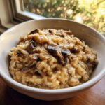 A close-up of a white bowl filled with rich, creamy mushroom risotto, topped with saut&eacute;ed mushrooms.