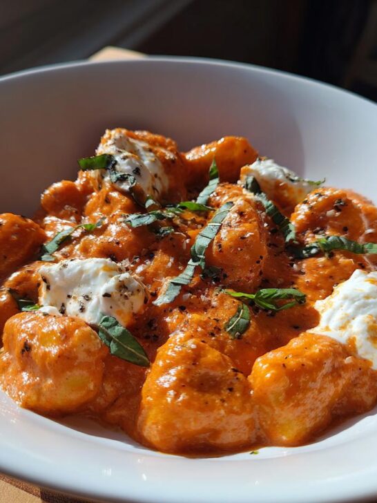 Close-up of Creamy Tomato Gnocchi With Burrata, topped with fresh basil and black pepper.