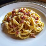 A close-up of creamy Tortellini Carbonara pasta topped generously with crispy bacon pieces and fresh black pepper.