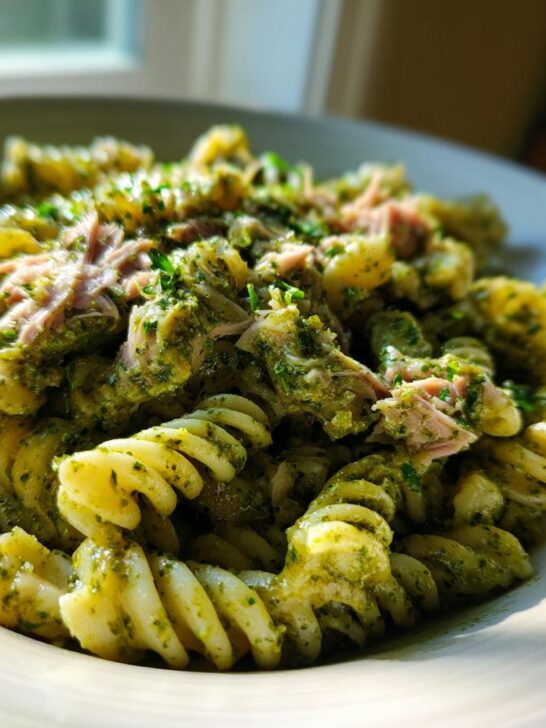 A close-up of a bowl filled with Creamy Tuna Pesto Pasta using fusilli noodles, topped with flaked tuna and parsley.