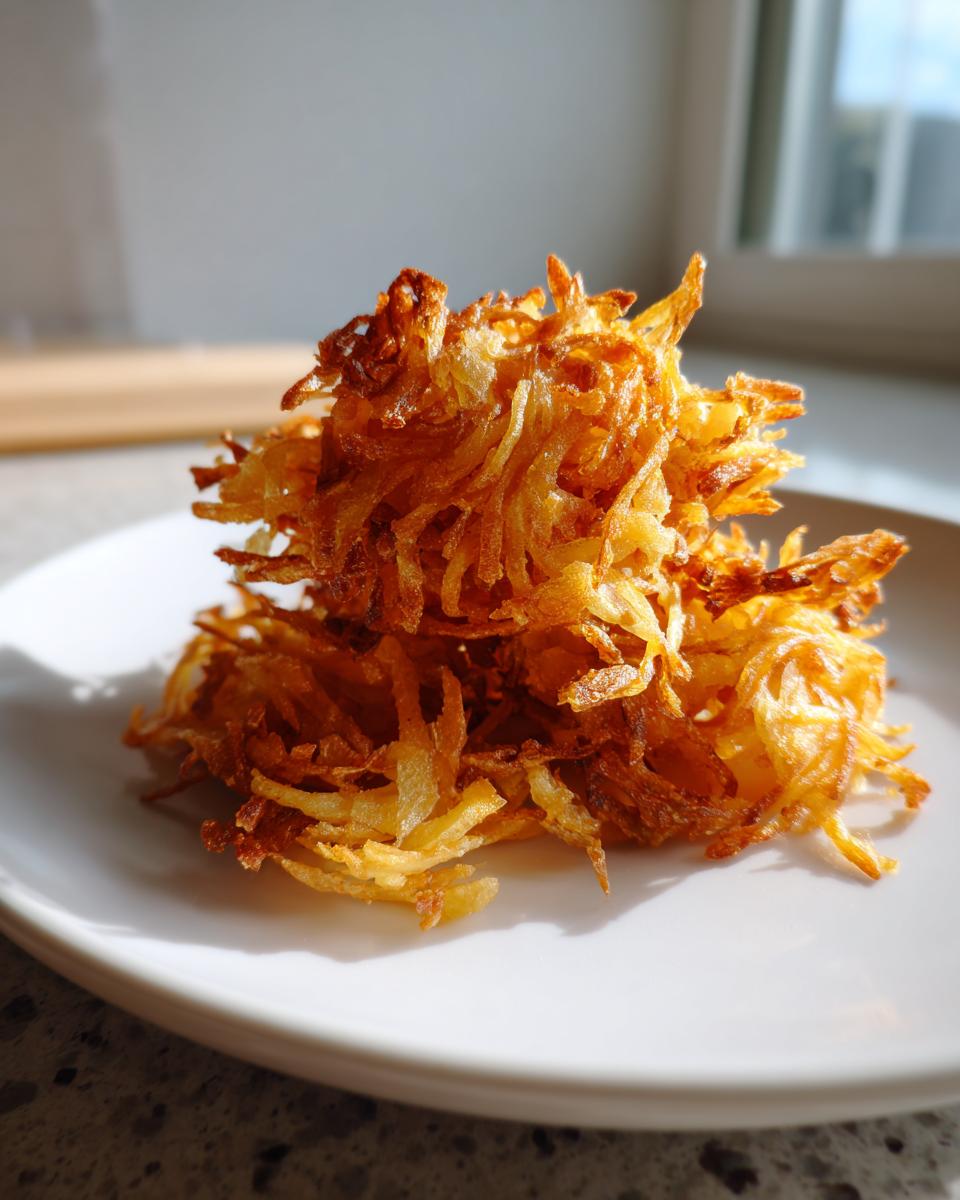 A close-up of crispy, golden brown Air Fryer Hash Brown Potatoes stacked high on a white plate.