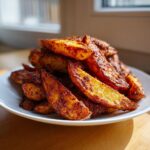 A close-up, appetizing photo of a mound of Crispy Baked Jerk Potato Wedges seasoned with spices, served on a white plate.