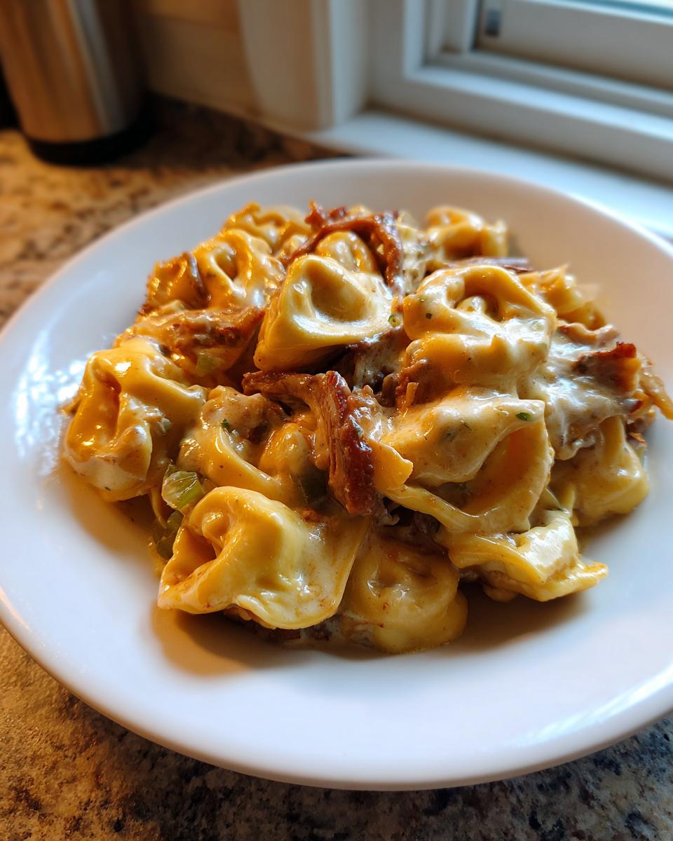 A close-up of a white bowl filled with creamy Crock Pot Cheesesteak Tortellini, topped with melted cheese and steak pieces.