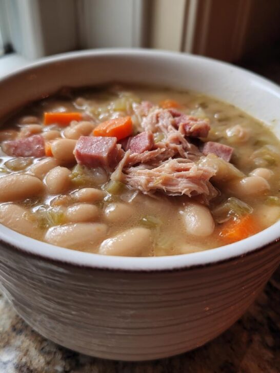 A close-up of a serving of Crockpot White Bean And Ham Soup, featuring white beans, shredded ham, and diced carrots.