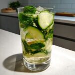 Close-up of a tall glass filled with a Cucumber Ginger Mint Mocktail, featuring cucumber slices, mint leaves, and bubbles.