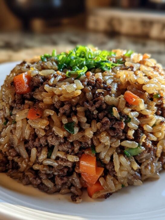 A perfectly molded mound of Dirty Rice With Ground Beef, garnished with fresh green onions, on a white plate.