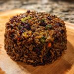 A perfectly molded serving of rich, dark Dirty Rice With Ground Beef, featuring visible grains, meat, and vegetables.
