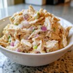 Close-up of shredded chicken salad mixed with red onion and green onions in a white bowl.