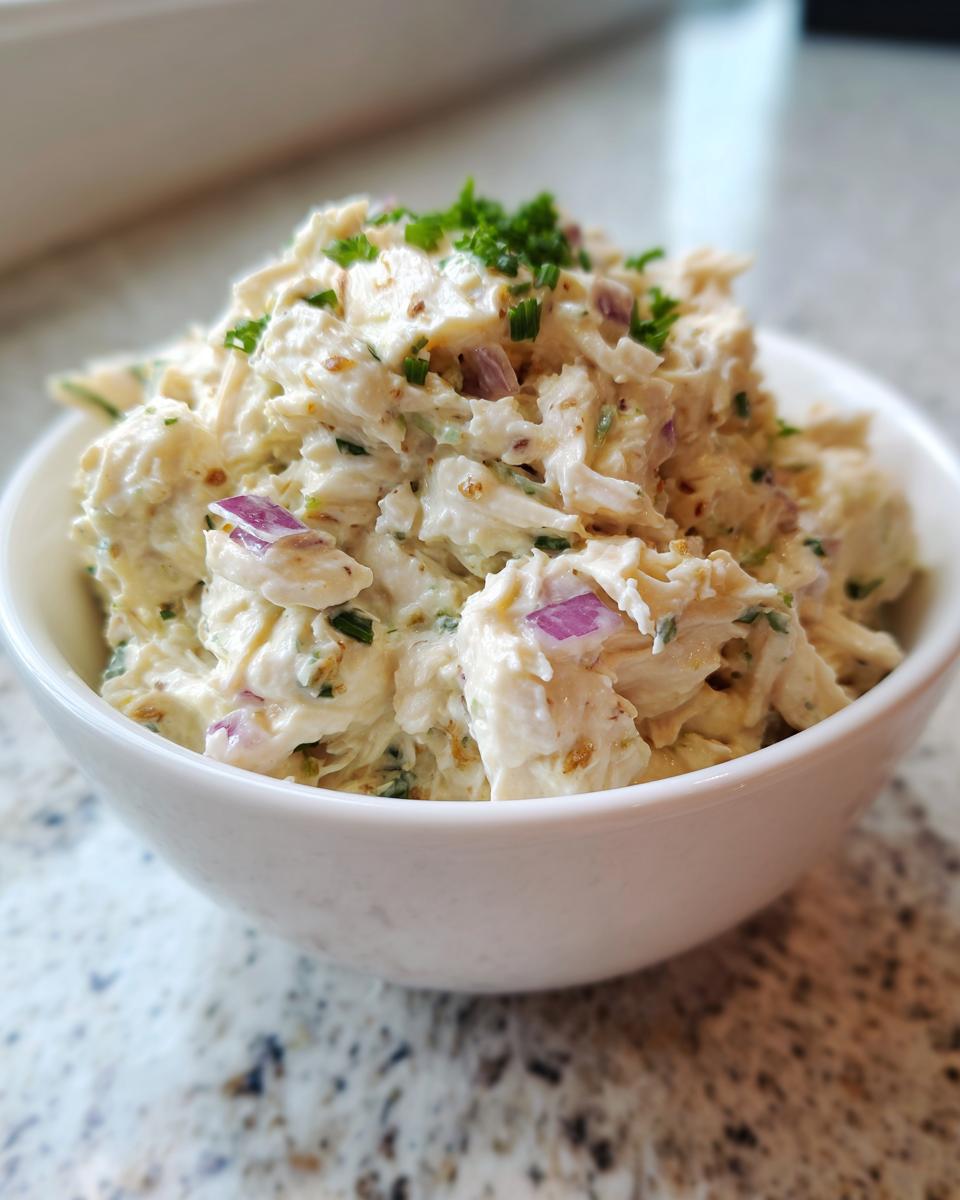A close-up of creamy Easy Chicken Salad Recipe Without Celery topped with fresh chives in a white bowl.