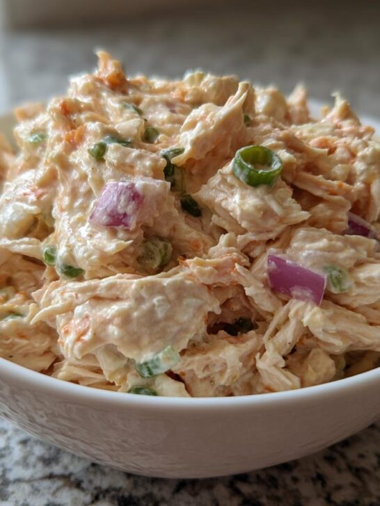 Close-up of creamy Easy Chicken Salad Recipe Without Celery mixed with red onion and green onions in a white bowl.