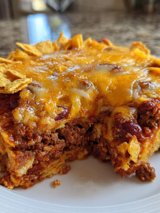 A thick slice of Easy Three Bean Taco Casserole topped with melted cheese and crushed tortilla chips.