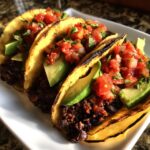 Three grilled corn tortillas filled with seasoned black beans, avocado slices, and fresh pico de gallo for Easy Vegan Black Bean Tacos.