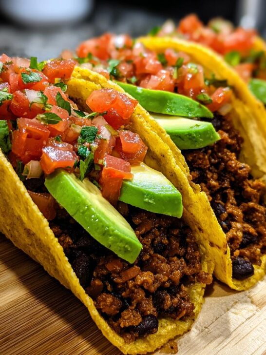 A row of Easy Vegan Black Bean Tacos filled with seasoned black bean mixture, avocado slices, and fresh pico de gallo.