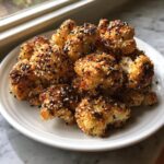A pile of golden-brown Everything Bagel Cauliflower Bites generously coated with black and white sesame seeds on a white plate.