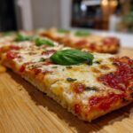 A close-up, low-angle shot of a slice of Flatbread Pizza Margherita with melted cheese and a fresh basil leaf.