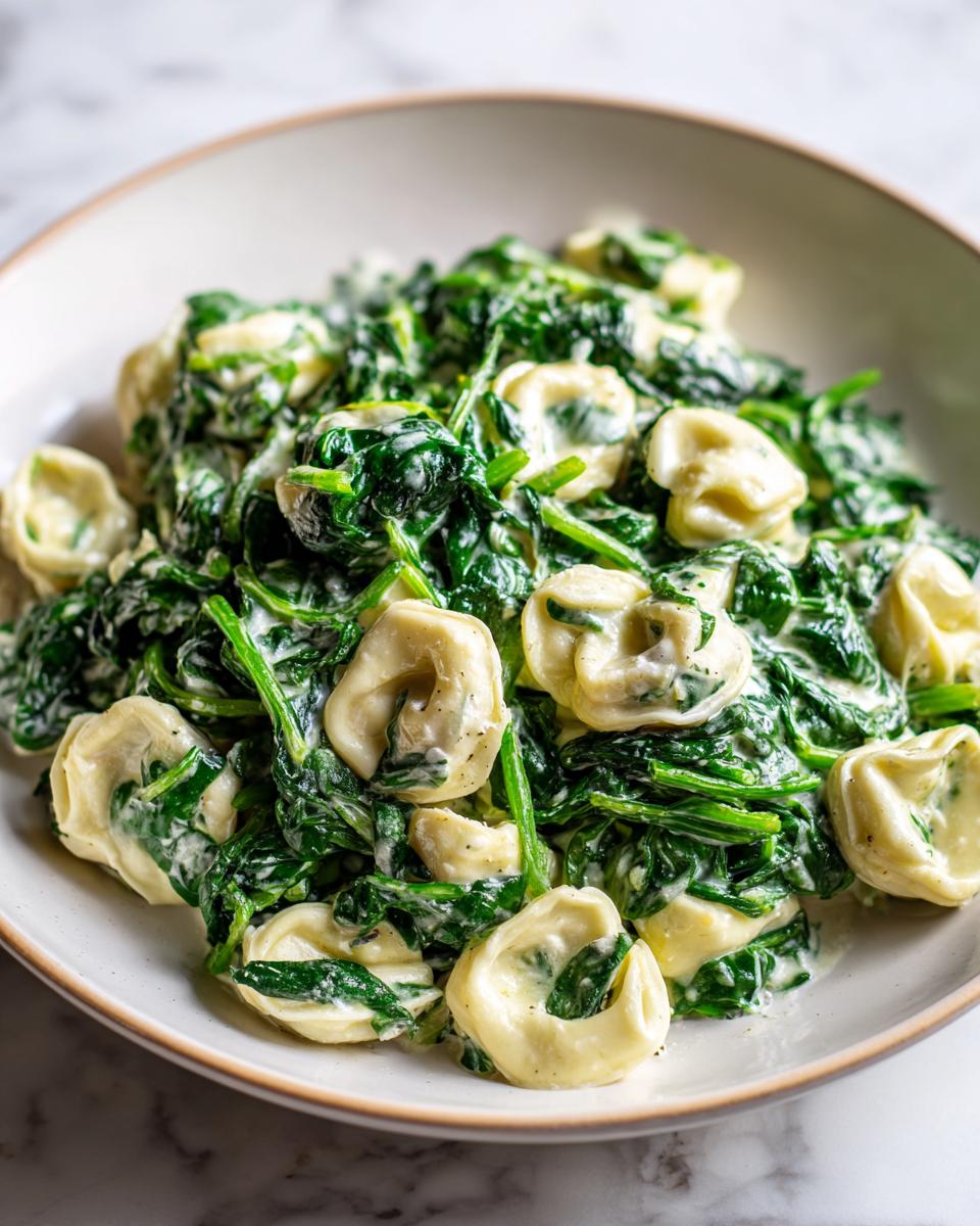 Close-up of creamy Garlic Spinach Tortellini tossed in a white, shallow bowl.