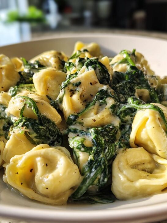 Close-up of creamy Garlic Spinach Tortellini tossed in a rich sauce, served in a white bowl.