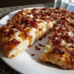 Close-up of a thick-crust Gluten Free Hot Honey Bacon Pizza slice showing melted cheese and drizzled honey.