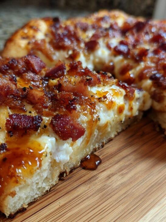 Close-up of a thick-crust Gluten Free Hot Honey Bacon Pizza slice showing melted cheese and drizzled hot honey.