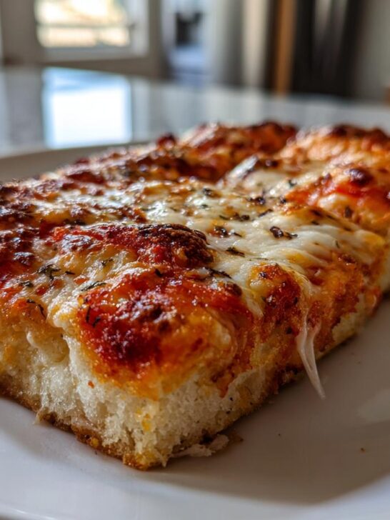 A thick, square slice of Grandmas Cheese Sheet Pan Pizza with bubbly, browned cheese on a white plate.
