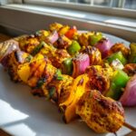 Close-up of grilled Greek Marinated Chicken Kabobs with charred chicken, red onion, and bell peppers on a white plate.
