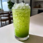 A tall glass filled with a vibrant Green Goddess Mocktail, featuring crushed ice and visible green flecks.