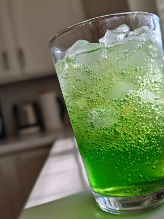 Close-up of a vibrant Green Goddess Mocktail filled with ice and carbonation bubbles.