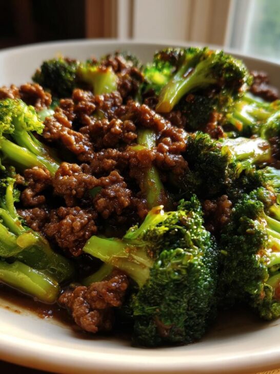 A close-up shot of a serving of Ground Beef And Broccoli Stir Fry coated in a savory brown sauce on a white plate.