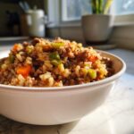 A white bowl filled with flavorful Ground Beef And Rice Skillet, mixed with diced carrots and green peppers.