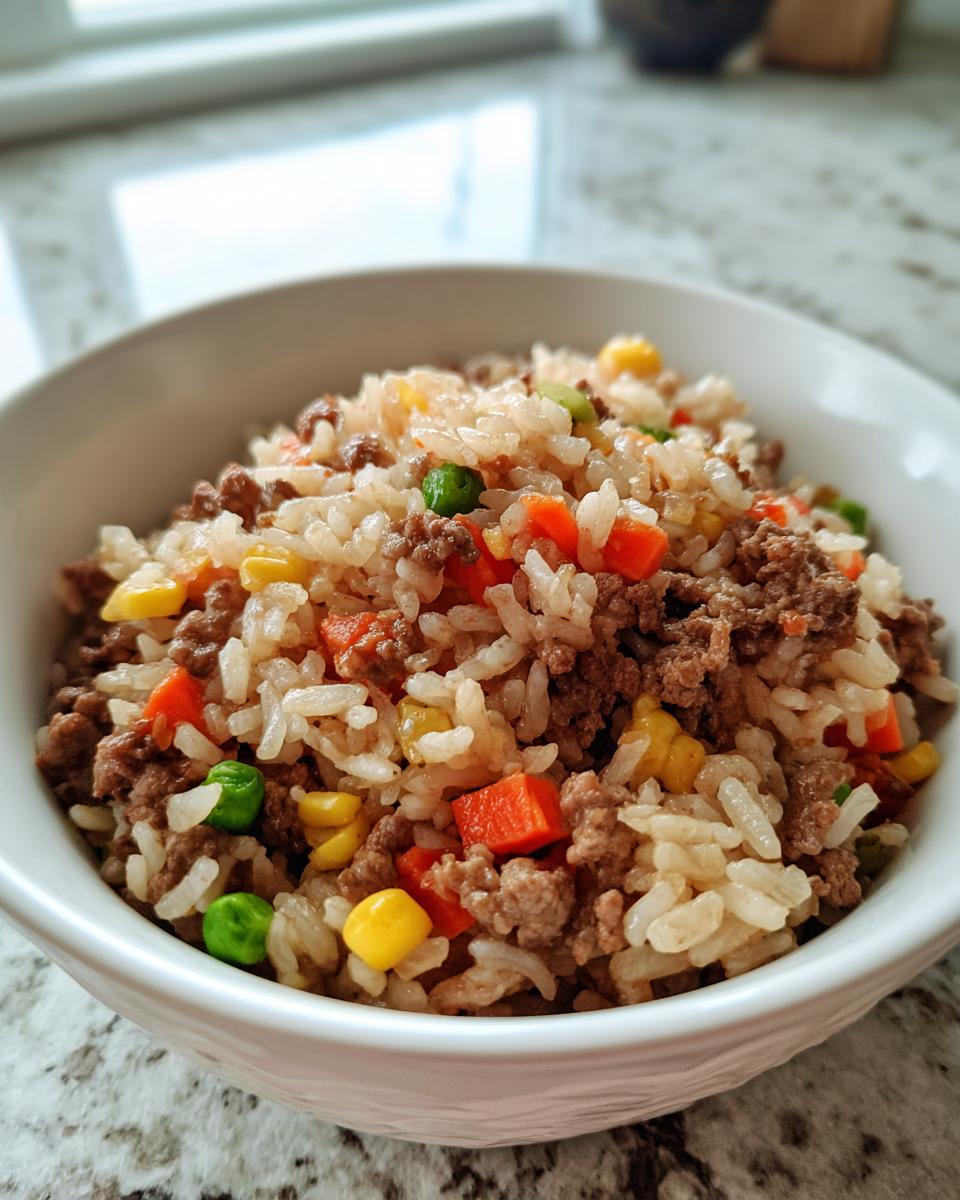 Close-up of a white bowl filled with Ground Beef And Rice Skillet mixed with peas, carrots, and corn.