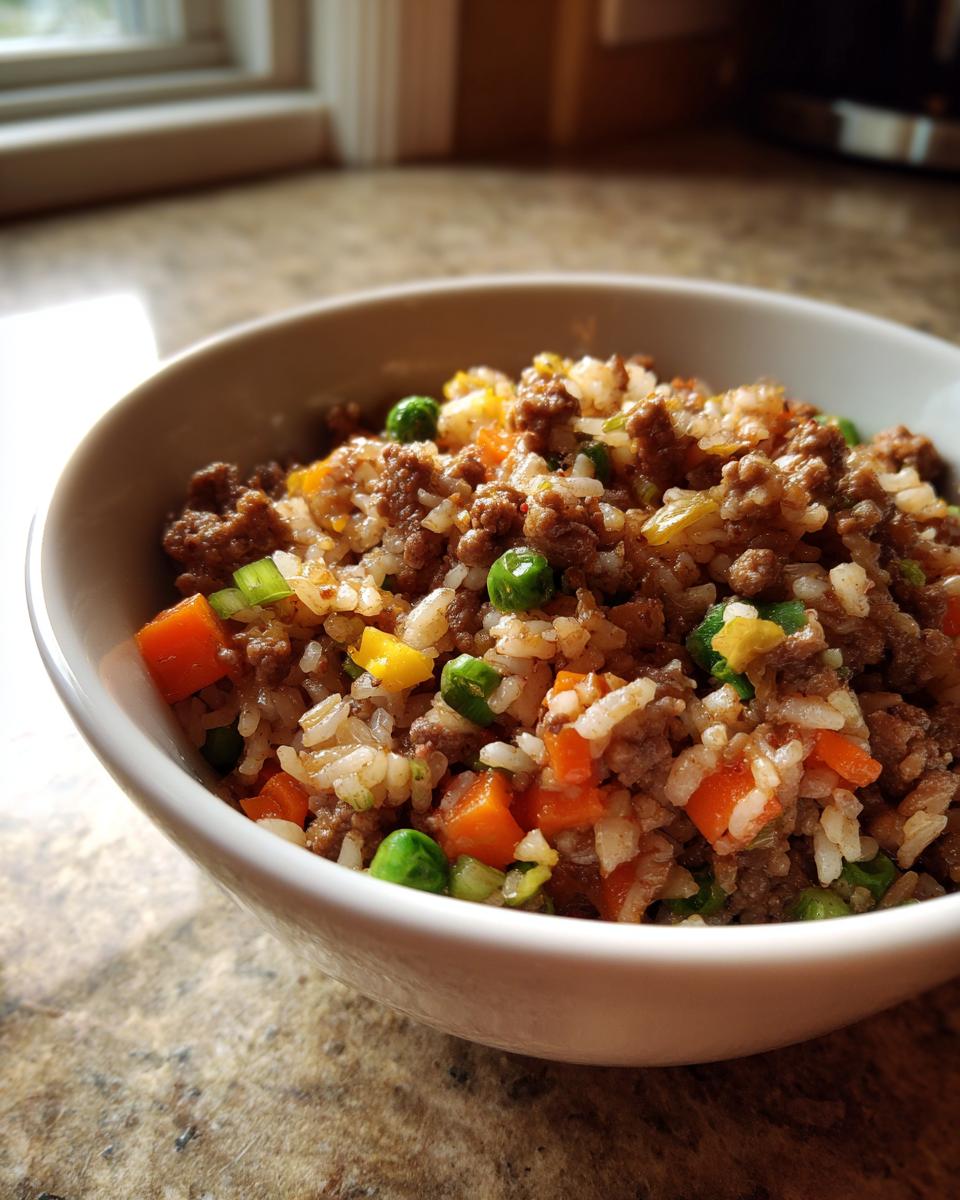 A close-up of a white bowl filled with Ground Beef And Rice Skillet mixed with peas, carrots, and scallions.