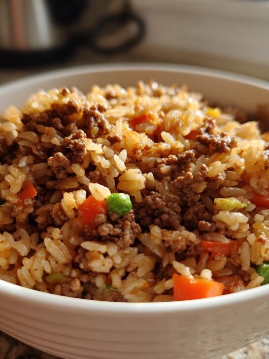 A close-up of a white bowl filled with Ground Beef And Rice Skillet mixed with peas and carrots.