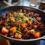Close-up of rich Ground Beef And Sweet Potato Skillet topped with fresh green onions in a dark skillet.